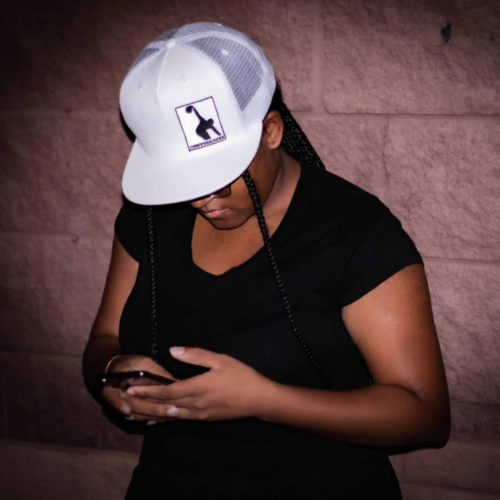 Person wearing a white cap with a logo against a brick wall.